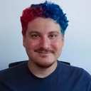 Erid Baldioceda smiling at the camera, with short curly hair dyed red and blue